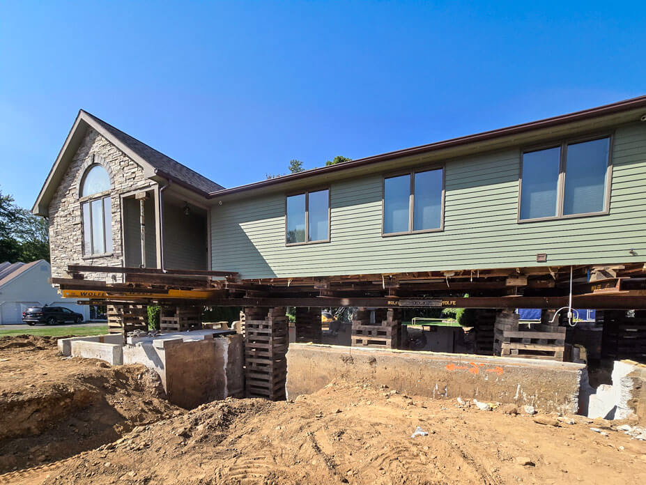 Green single story home elevated on cribbing for new foundation