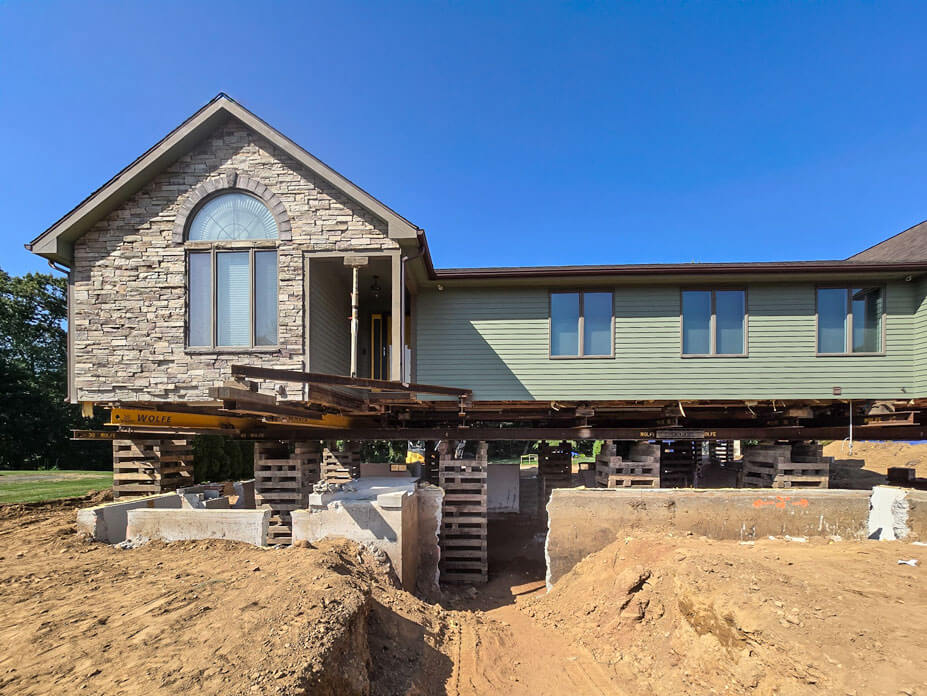 Front view of green and stone single story home elevated on cribbing 