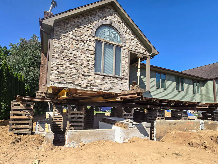 Single story stone and frame house elevated on cribbing to replace failing foundation