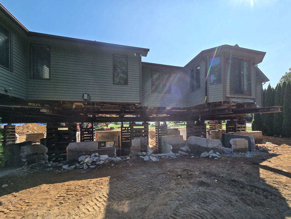 House sits elevated on cribbing while old foundation is removed for replacement