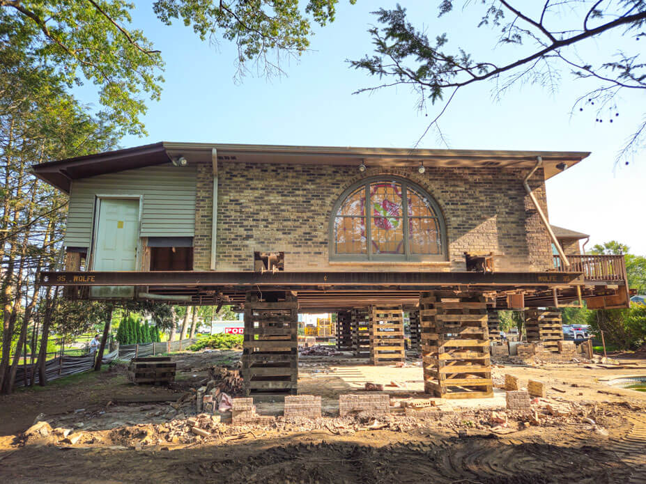 Brick and frame house with stained glass window sitting on cribbing and steel for new basement