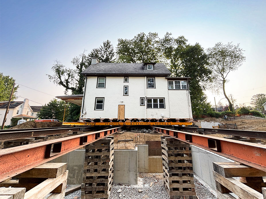 White house sits on steel beams in background with roll beams and cribbing in foreground