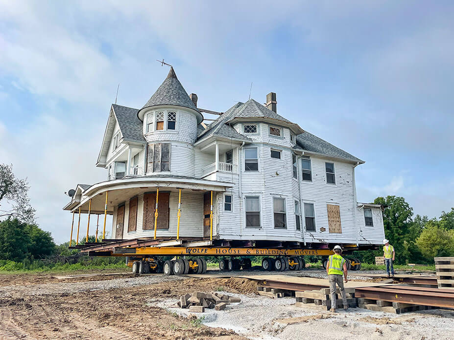 A worker looks on as a white house on house moving dollies rolls up to new foundation