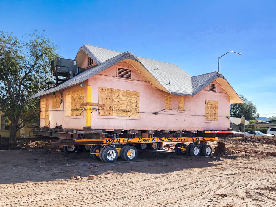 Pink stucco bungalow sits on Wolfe steel and dollies ready for relocation