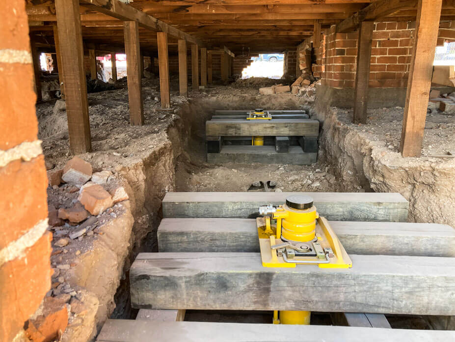 Crawlspace of brick house with cribbing and crib jacks in preparation for lifting