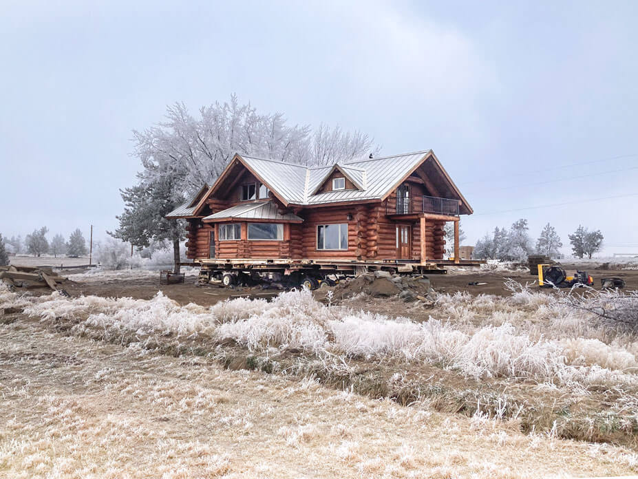 Log cabin on dollies for relocation with frost-covered grass in foreground