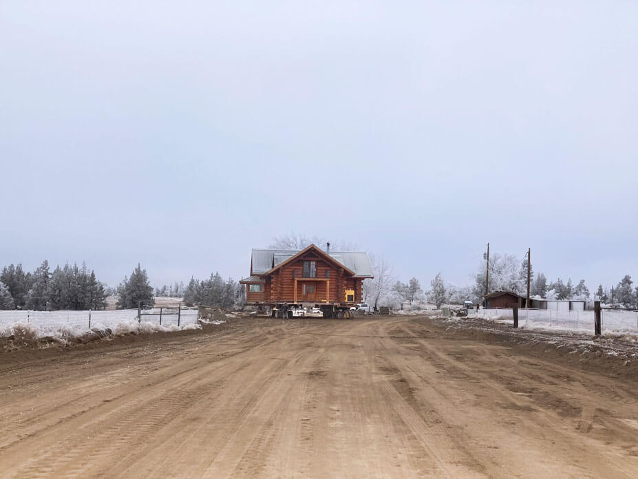 Wolfe drives a log cabin down a dirt road with snowy fields on each side