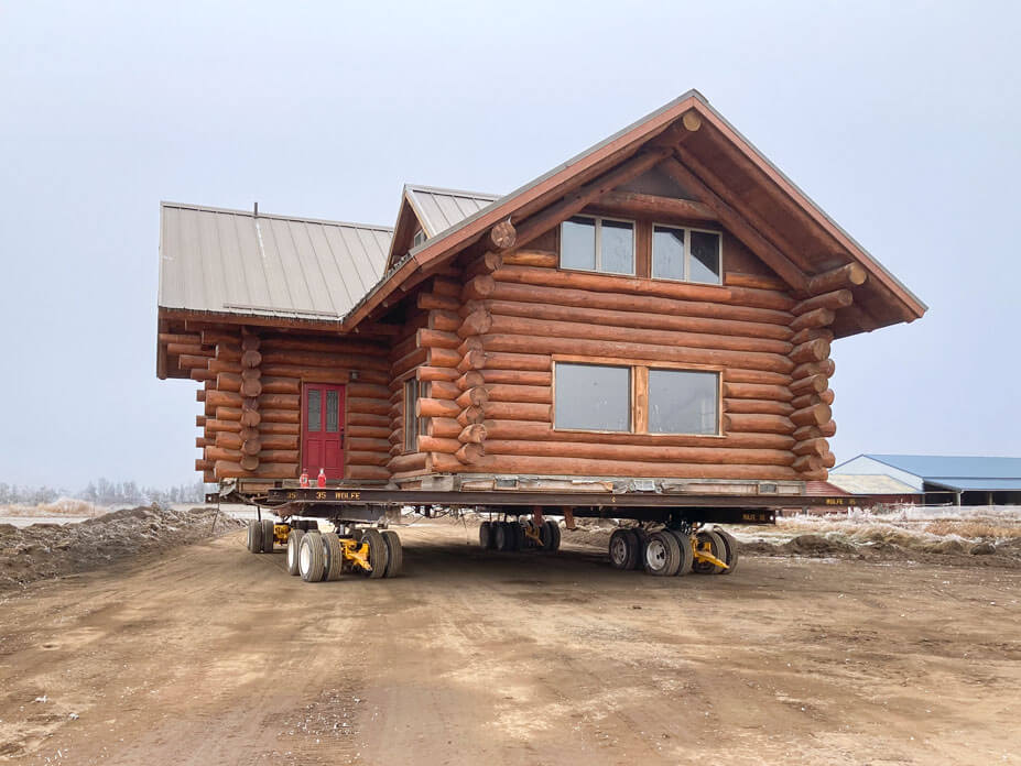 Front view of two-story log cabin in road as Wolfe House Movers drives it to new location